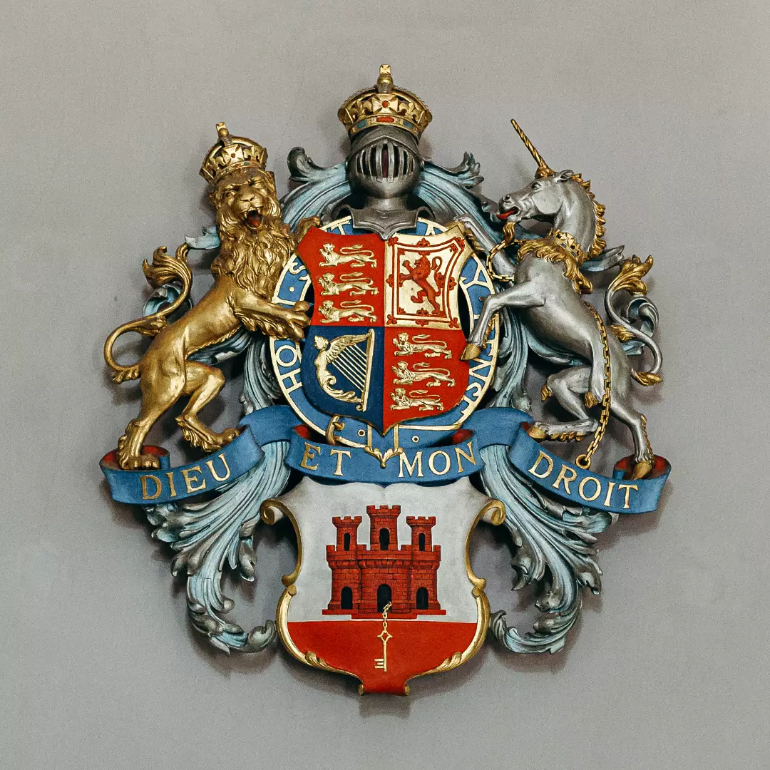 A heraldic coat of arms featuring a crowned lion, a crowned unicorn, and a shield with multiple emblems; text banners read 