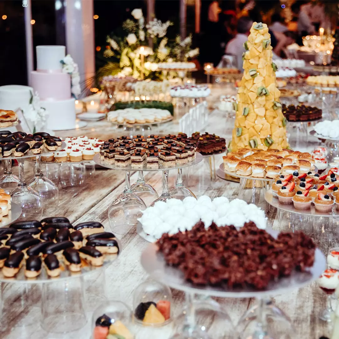 A large assortment of desserts, including pastries, cakes, and fruit tarts, is arranged on a wooden table at an event or reception.